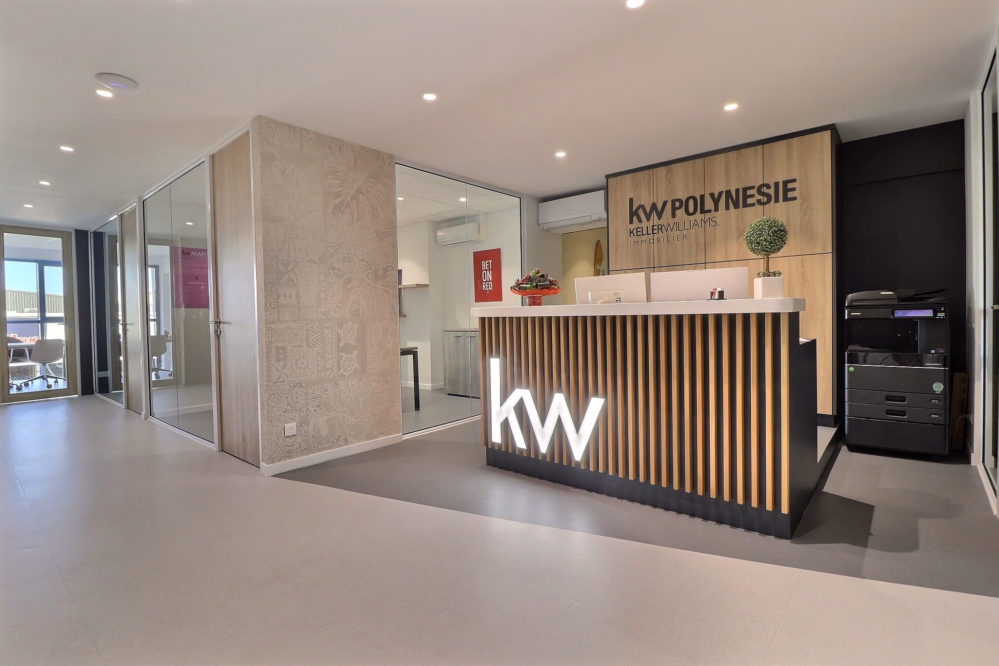 L’accueil du Market Center KW Polynésie : comptoir en tasseaux de bois, logo kw rétroéclairé, salles de réunion vitrées